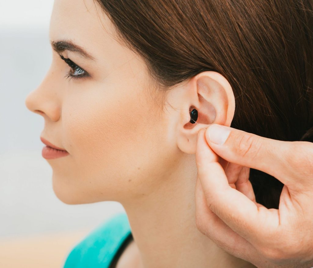 A woman is having an in-ear hearing aid adjusted by a professional