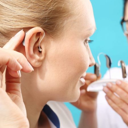 A woman is inserting a hearing aid with guidance from an audiologist